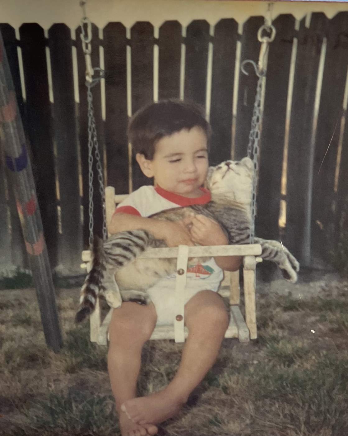 Adam de niño en un columpio, abrazando a un gato